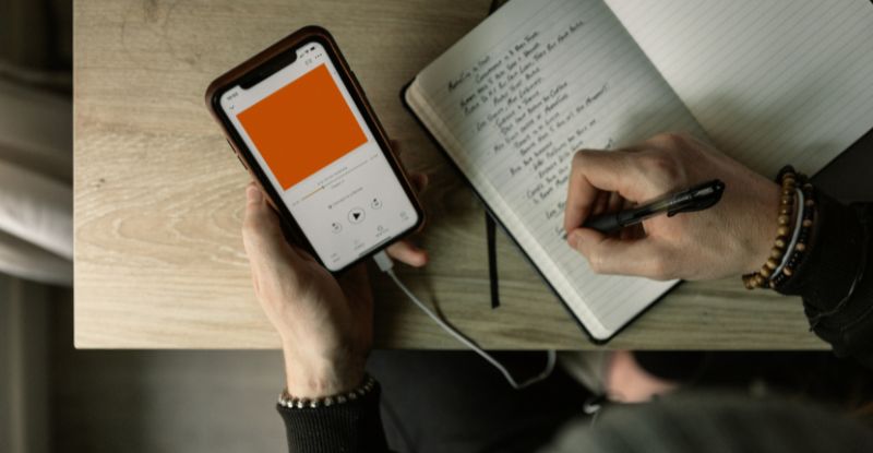 Person listening to podcast and taking notes
